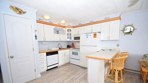A kitchen with white cabinets, a wooden countertop, and a small island with chairs. - Eldorado 2 - Ocean City, MD (Ocean City)