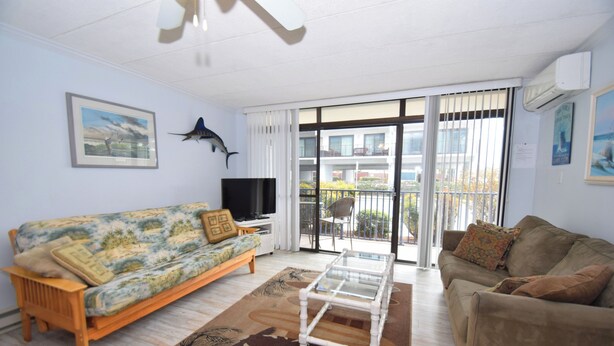 A living room with a sofa, a coffee table, a TV, and a balcony with a view. - Eldorado 2 - Ocean City, MD (Ocean City)