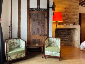 A traditional room with exposed wooden beams, a fireplace, two floral-patterned chairs, and a red lamp. - Quaint 1-bedroom cottage in Livarot-Pays-d'Auge perfect for relaxing (Livarot-Pays-d'Auge)