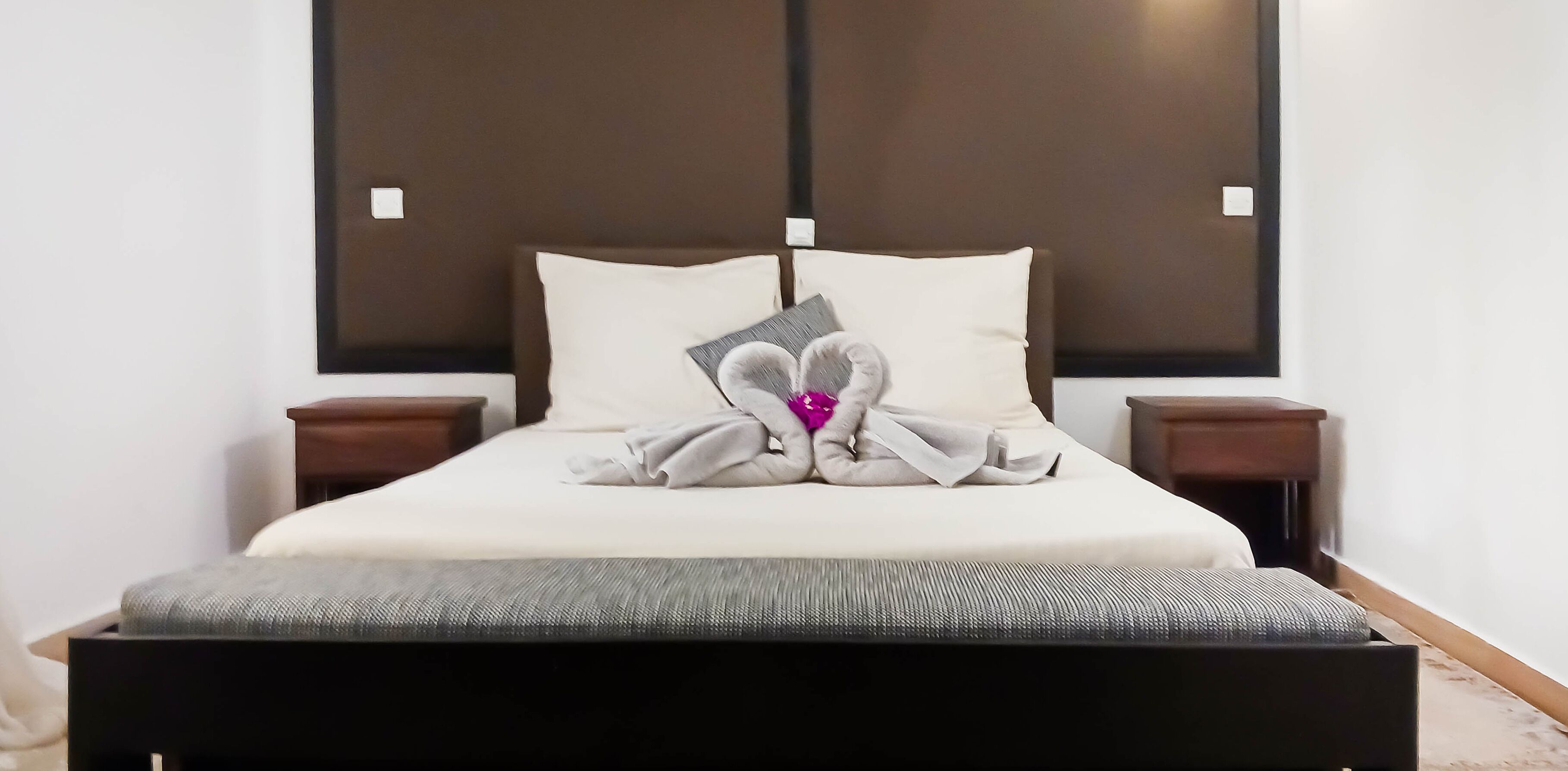 A neatly made bed with pillows, a bedside table, and a headboard.