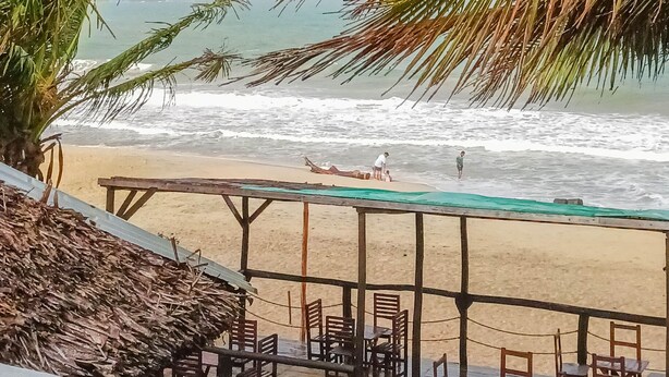 A beach view with a table and chairs, palm trees, and a rainbow.