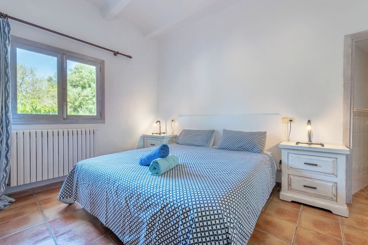 Un dormitorio con una cama, dos mesitas de noche, un ventanal y un radiador.
