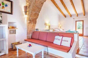A cozy room with a stone arch, a red sofa with white pillows, a white table, and a bed with a blue blanket. - Agroturismo Es Rafal Roig by MHR (Manacor)