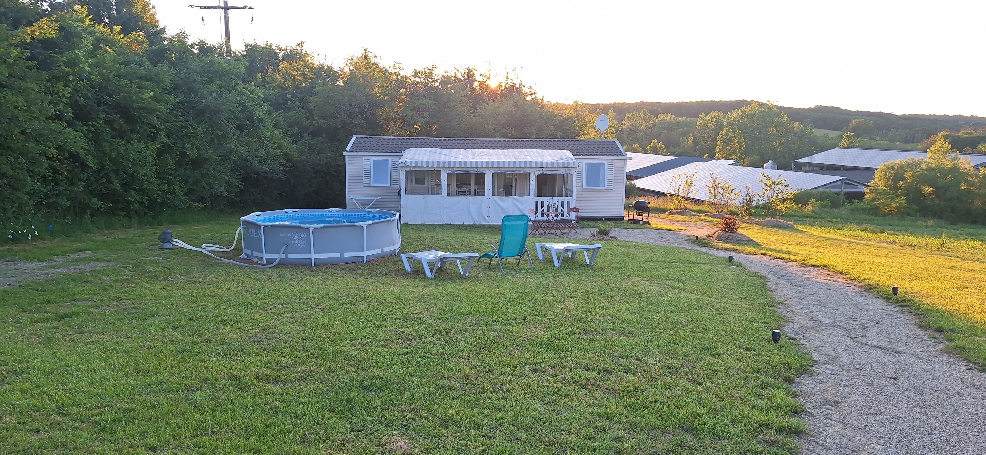 A mobile home with a swimming pool, outdoor seating, and a path leading to other homes.