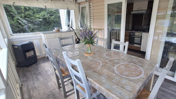 A dining area with a table, chairs, a vase with flowers, and a view of a kitchen and outdoors. - Comfortable mobile homes (Bourgougnague)