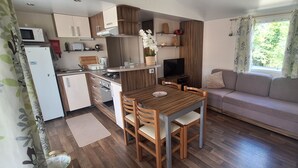 A compact kitchen with a dining table and chairs, a sofa, and a TV. - Comfortable mobile homes (Bourgougnague)
