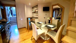 Un espace repas moderne avec une table en verre, des chaises blanches et un téléviseur à écran plat fixé au mur.