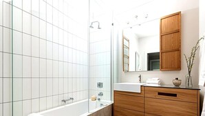 Un bagno moderno con cabina doccia in vetro, una vasca freestanding, un mobile bagno in legno con specchio e un water bianco.