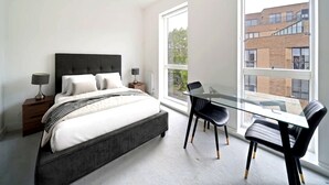 Una camera da letto con un letto, comodini, un tavolo in vetro con sedie e un'ampia finestra.