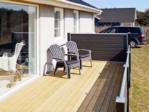 A deck with two Adirondack chairs, a glass door, and a vehicle parked in the background. - 4 Star Holiday Home in Lokken (Lokken)