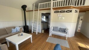 A cozy room with a white sofa, a white table, a wooden floor, a loft with a wooden beam, and a black stove. - 4 Star Holiday Home in Lokken (Lokken)