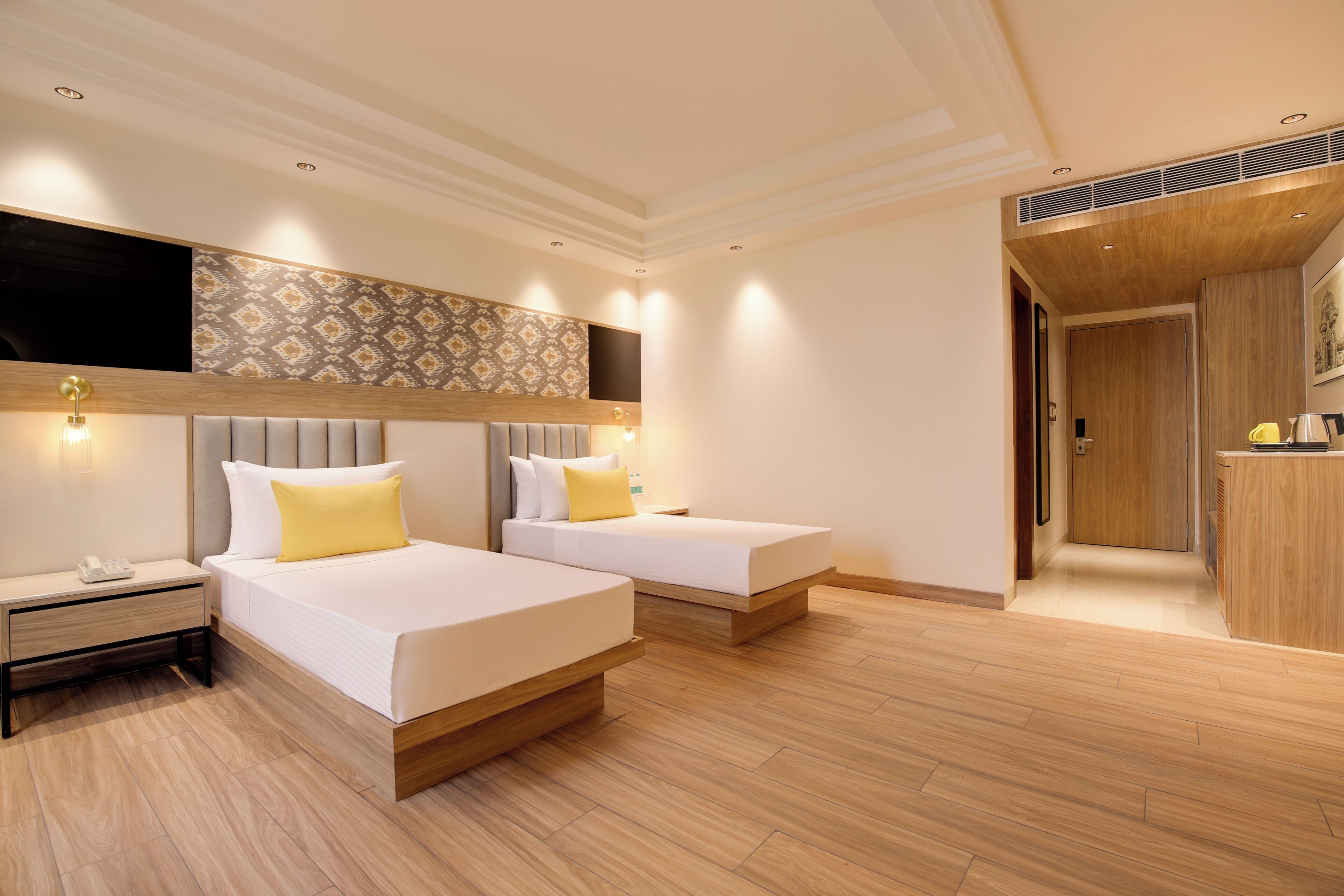 Habitación de hotel con dos camas, un televisor montado en la pared, piso de madera y una zona de kitchenette.