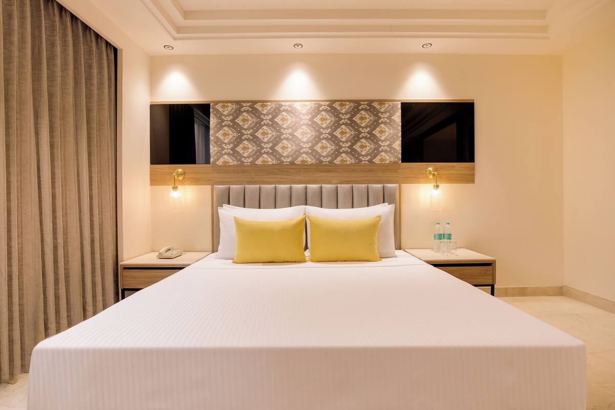 A hotel room with a large bed, a headboard with a patterned design, two bedside lamps, a nightstand with a phone, and a wall-mounted TV.