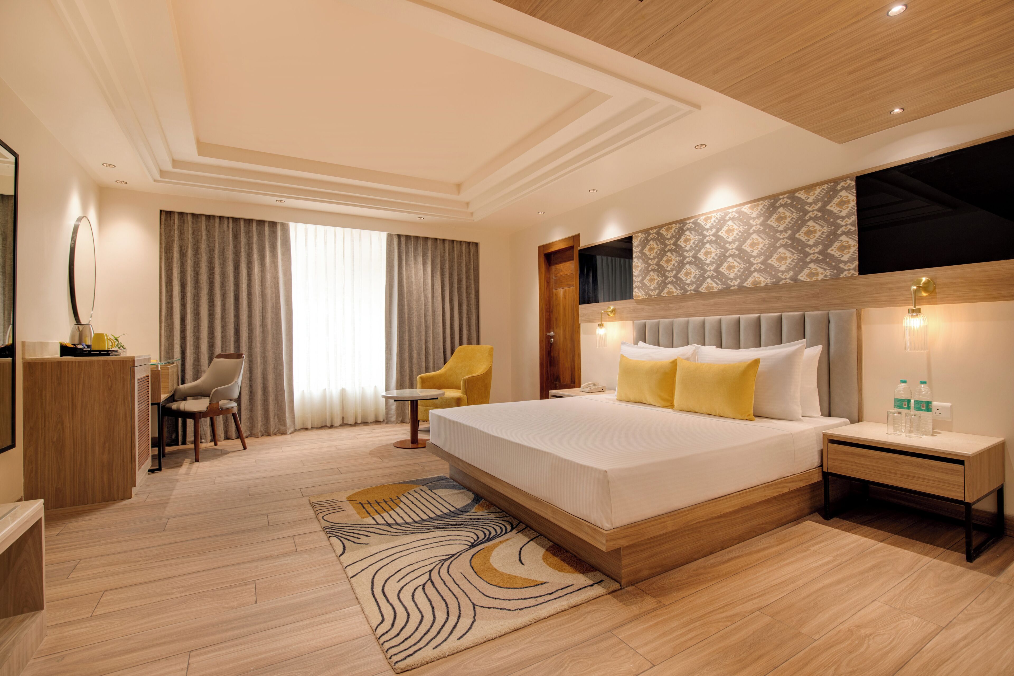 A modern hotel room with a large bed, a desk, a chair, and a small table.