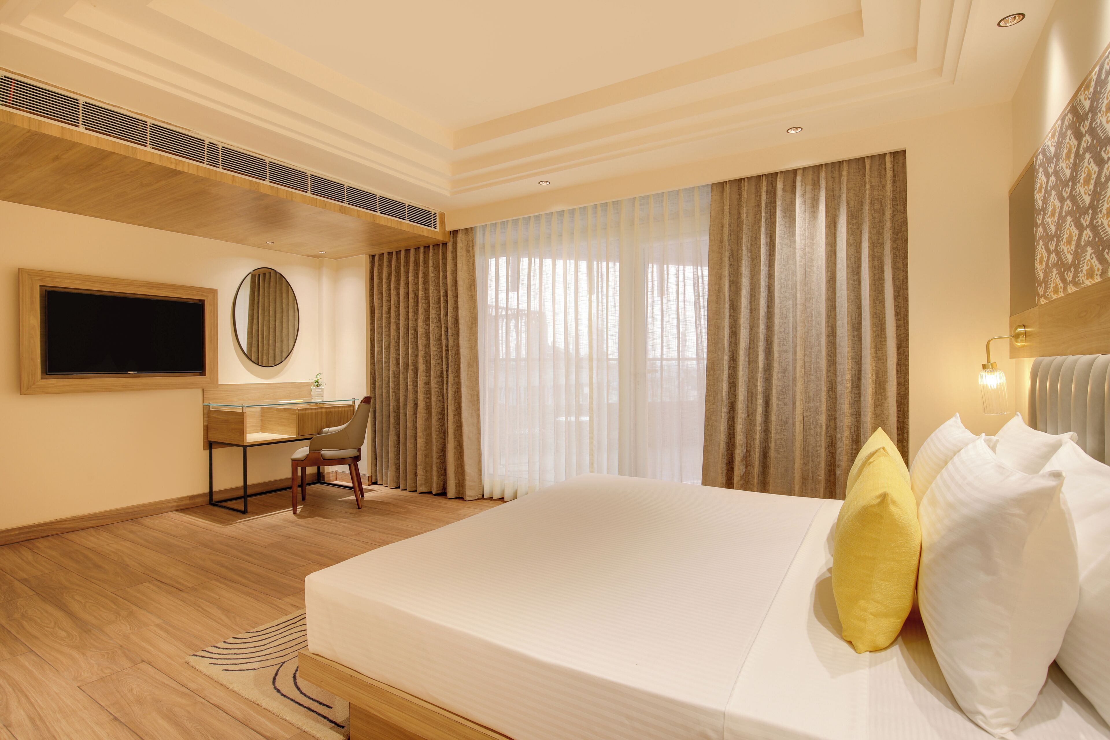 A hotel room with a bed, a desk, a chair, a TV, and a large window with curtains.