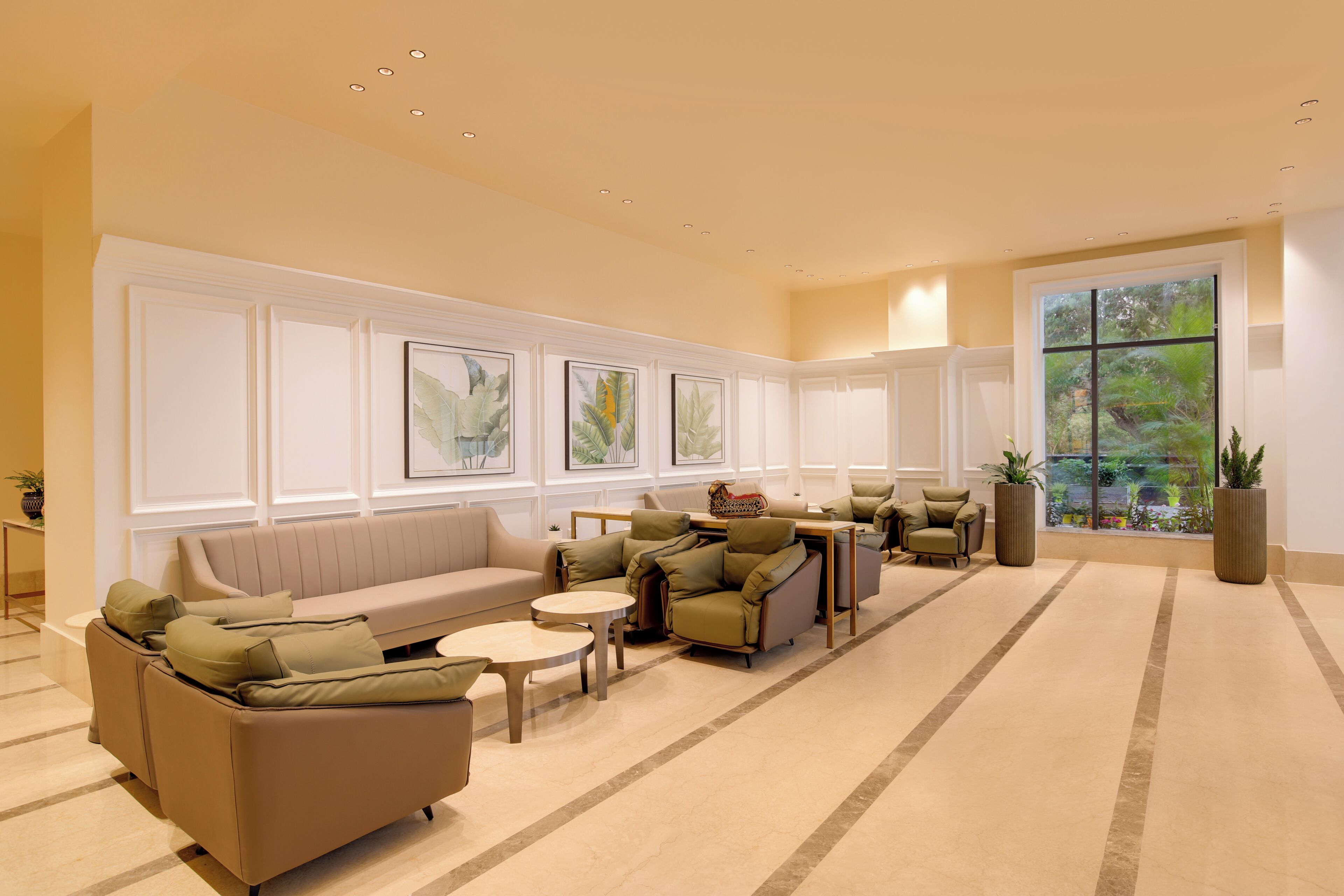 Un hall d’entrée spacieux, avec un canapé beige, des fauteuils, une table basse et une grande fenêtre donnant sur un paysage verdoyant.