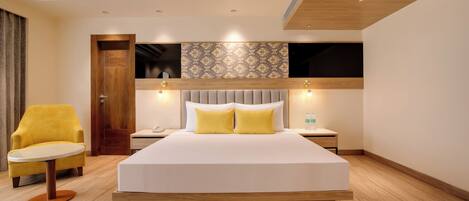 Habitación de hotel moderna con una cama grande, un sillón amarillo, una mesita de noche y un televisor de pared.