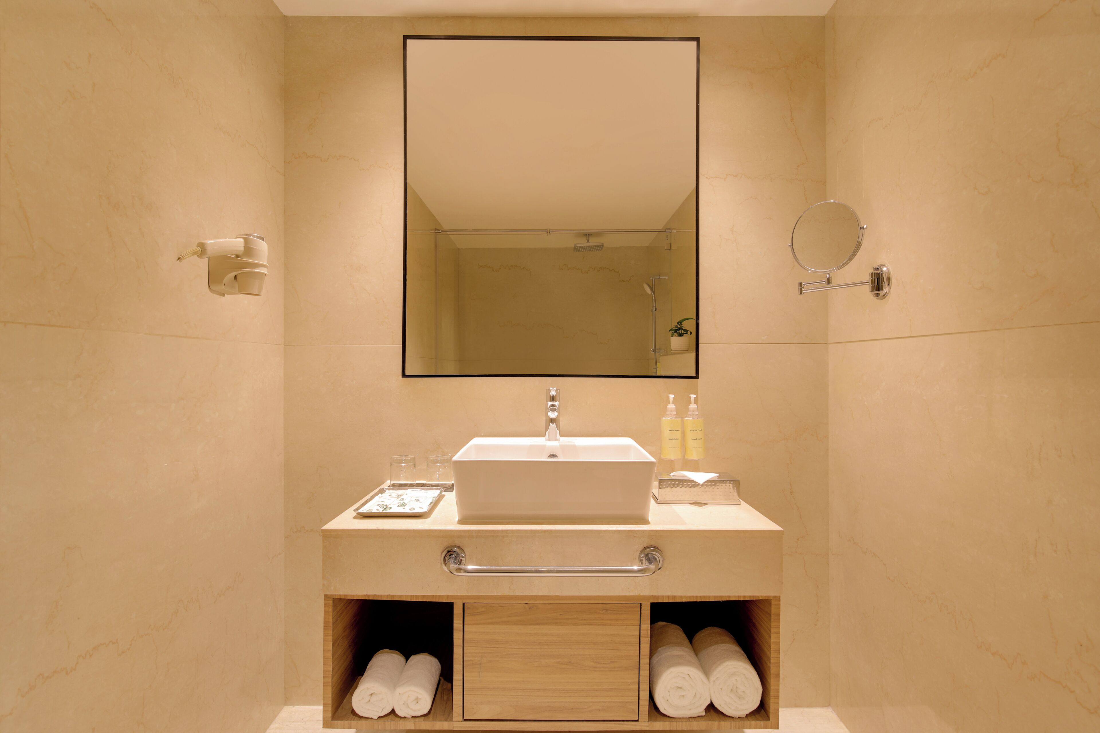 Une salle de bain équipée d’un lavabo, d’un miroir, d’un distributeur de serviettes et d’une petite étagère contenant des articles de toilette.