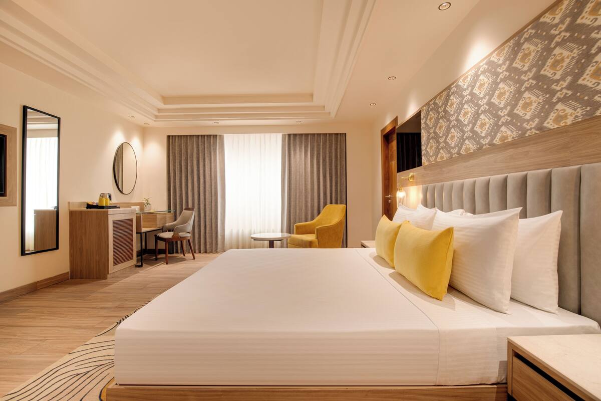 A hotel room with a large bed, a desk, a chair, a small table, and a mirror.