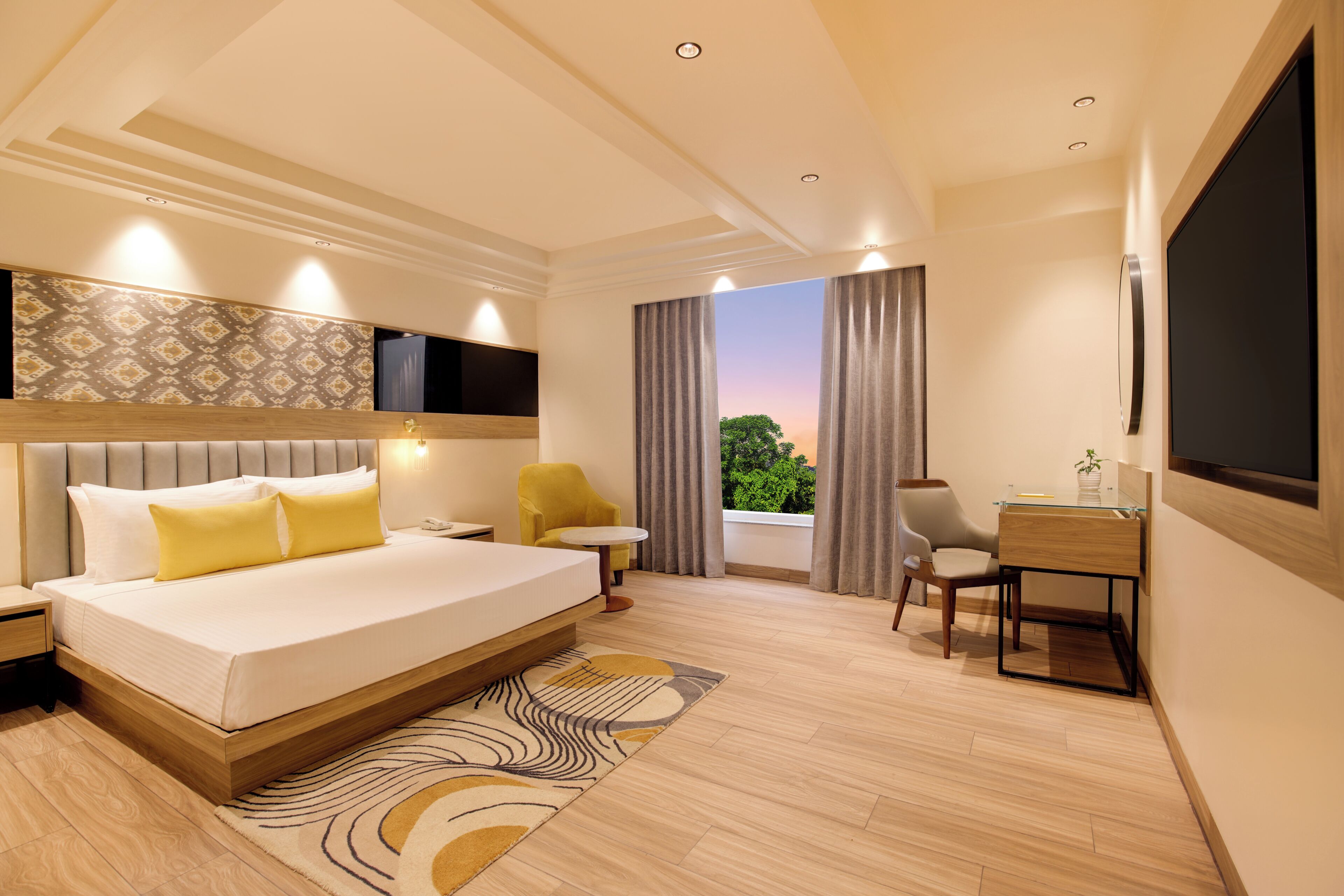 A modern hotel room with a large bed, a desk, a chair, a TV, and a window with curtains.