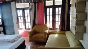 A hotel room with a bed, a sofa, a chair, and a window with curtains. - Hotel City Plaza Dharamshala (Dharamshala)
