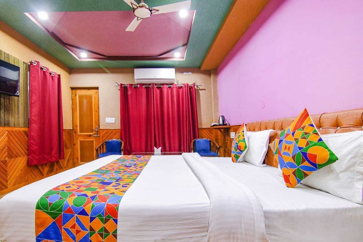 Ein Hotelzimmer mit Bett, Schreibtisch, Stuhl, Deckenventilator und roten Vorhängen.