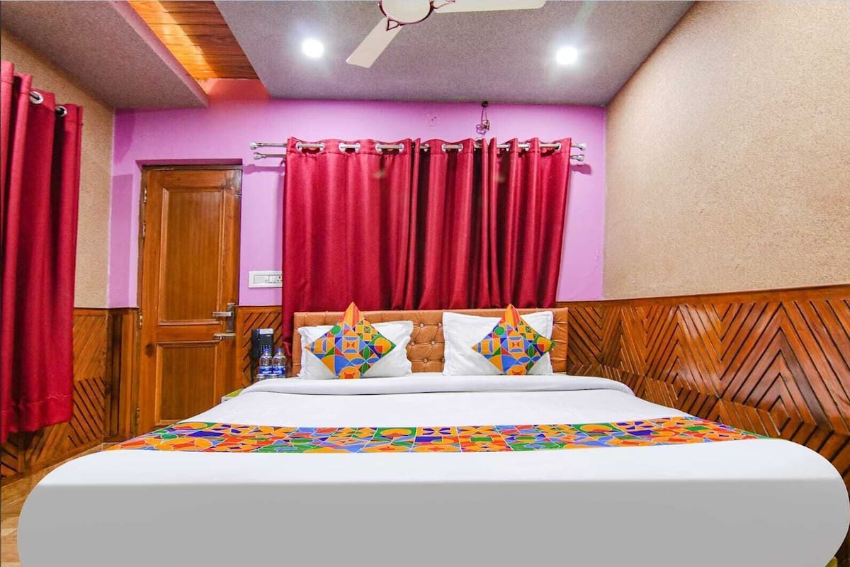 Ein Hotelzimmer mit Bett, roten Vorhängen, einem Holzkopfteil und einem Deckenventilator.
