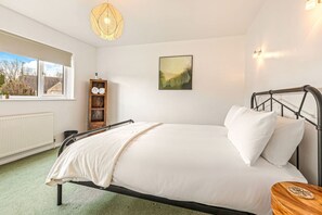 A bedroom with a bed, a bedside table, a window, a radiator, and a shelf with towels. - The Wild Duck in Bourton-On-The-Water (Bourton-on-the-Water)