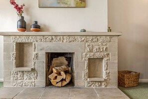 A stone fireplace with a fire, a vase with flowers, and a painting on the wall. - The Wild Duck in Bourton-On-The-Water (Bourton-on-the-Water)