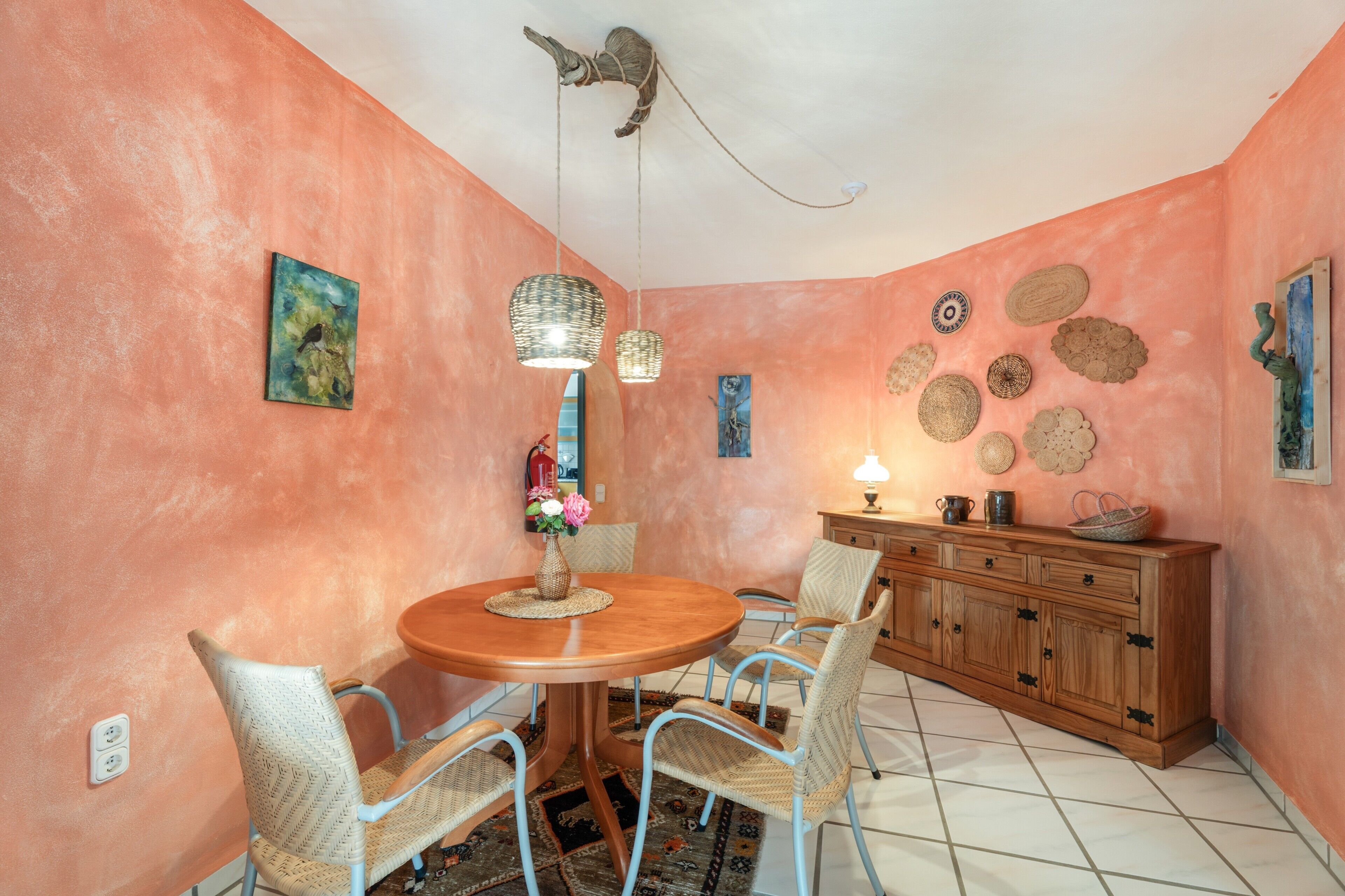A dining area with a round table, wicker chairs, a wooden cabinet, and decorative wall hangings.