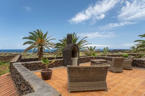 A patio with wicker furniture, a stone structure, and palm trees.