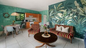 Ein Wohnzimmer mit rundem Tisch, gestreifter Couch und einer großen, tropischen Wandmalerei.