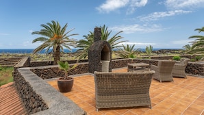 Eine Terrasse mit Korbmöbeln, einer Steinstruktur und Palmen.