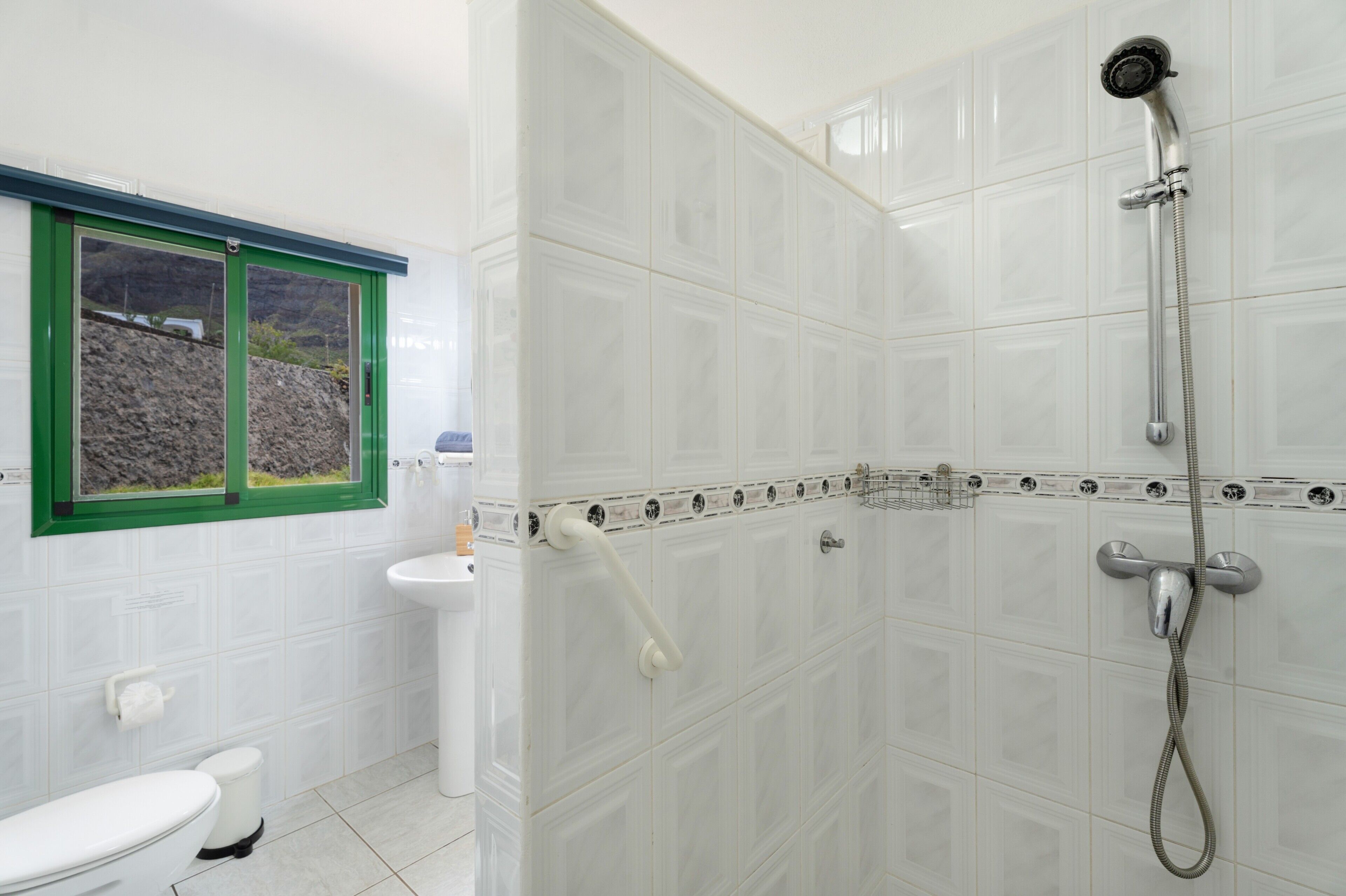 A bathroom with a toilet, sink, shower, and a window with a green frame.