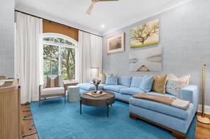 A living room with a blue sofa, a round coffee table, and a view of trees through a large window.