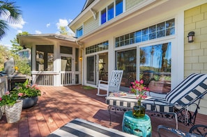 A covered patio with outdoor furniture, a grill, and potted plants.