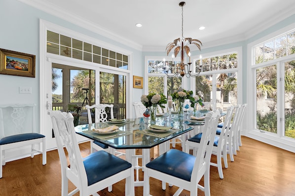A dining area with a glass table, white chairs, and a chandelier.