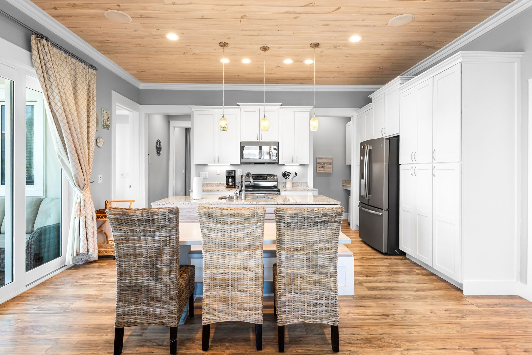 Een moderne keuken met witte kasten, een centraal eiland met stoelen en een houten plafond.
