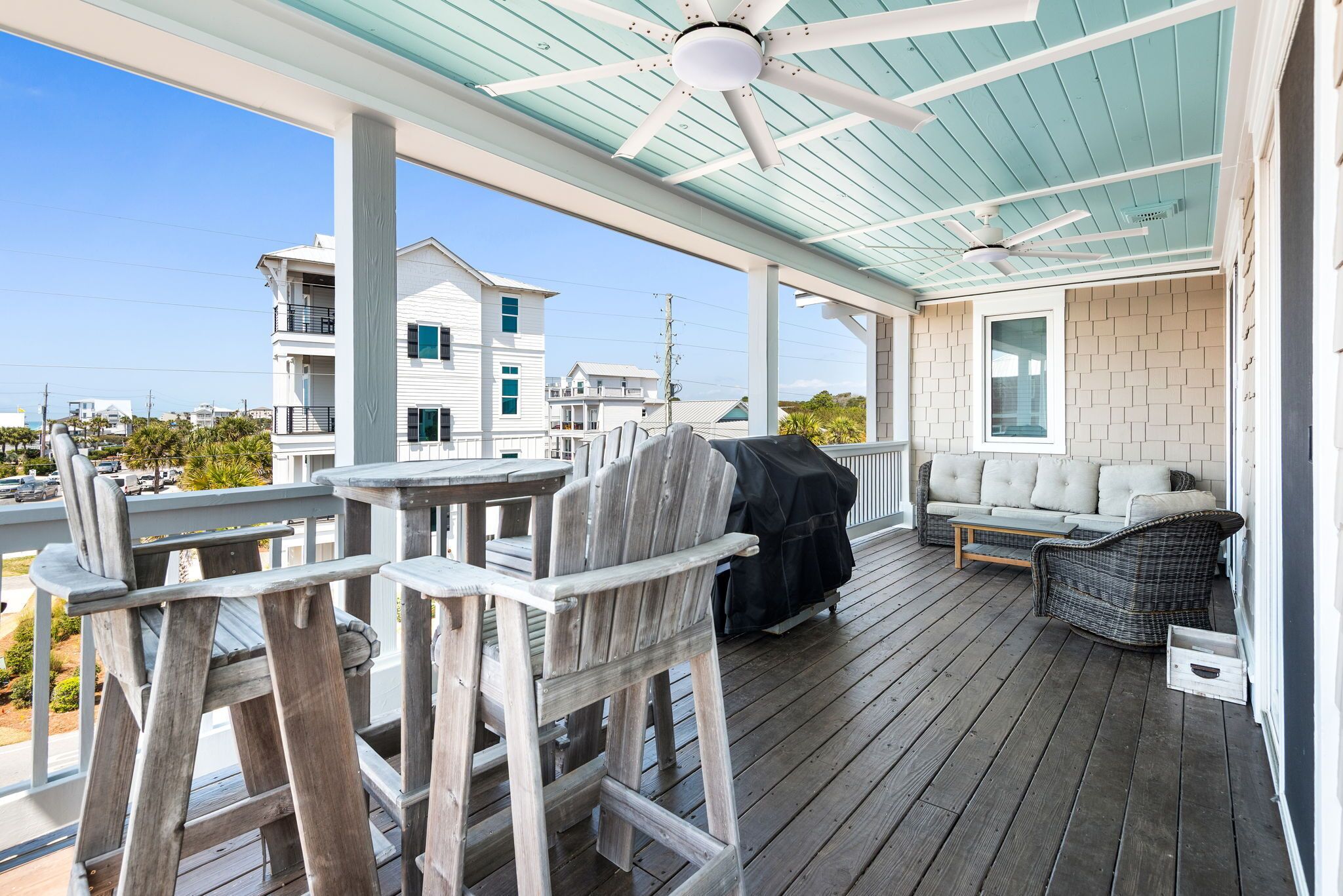 A covered outdoor deck with wooden chairs, a barbecue grill, and a sofa.