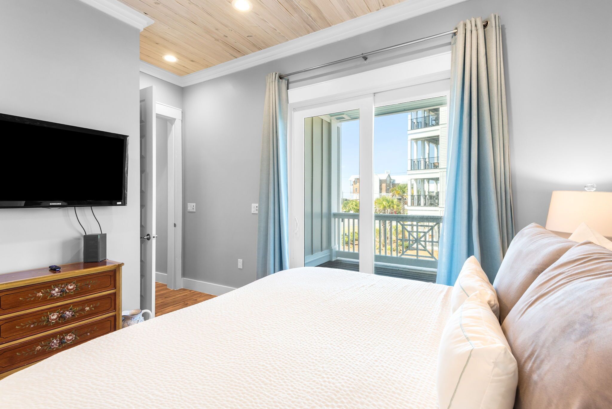 Une chambre à coucher comprenant un lit, une commode, un téléviseur et un balcon avec des rideaux.