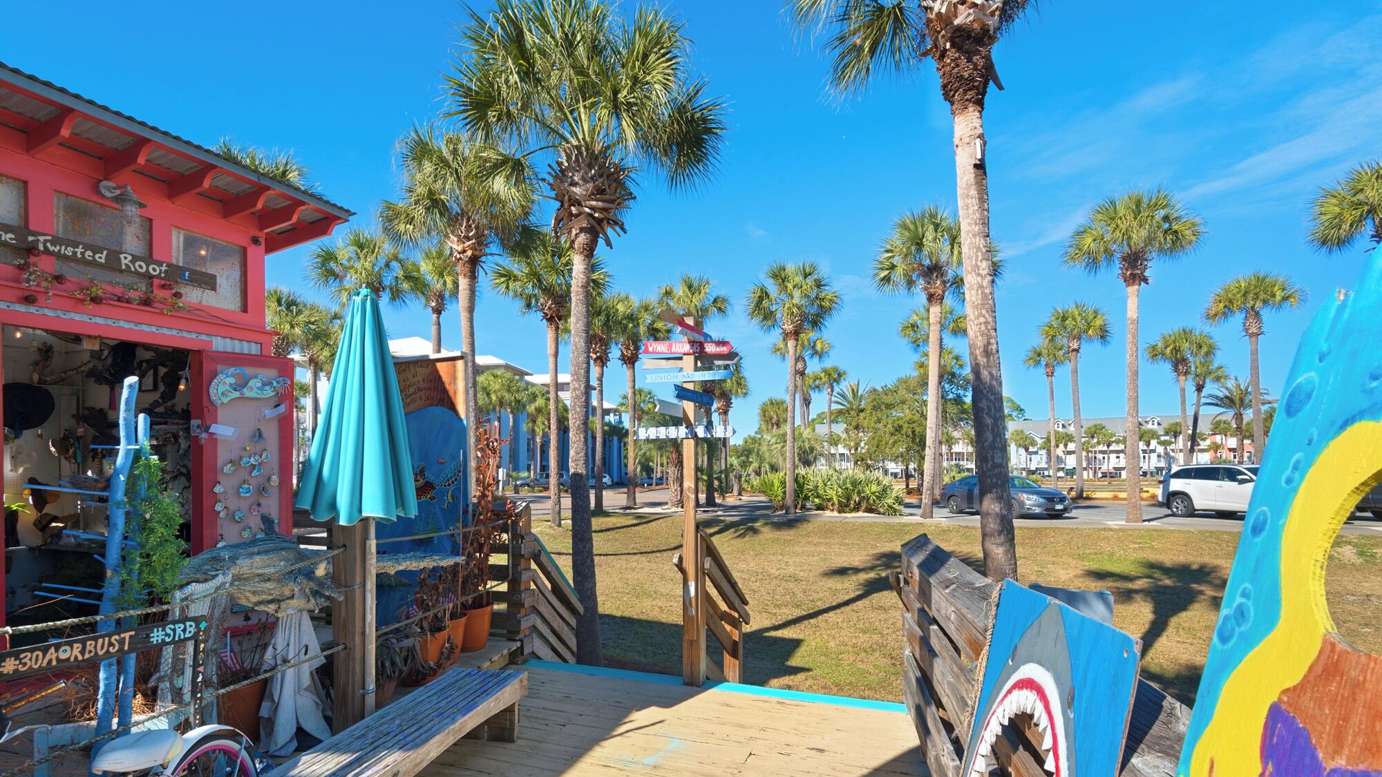 A colorful outdoor area with a wooden deck, palm trees, and a signpost with directions.