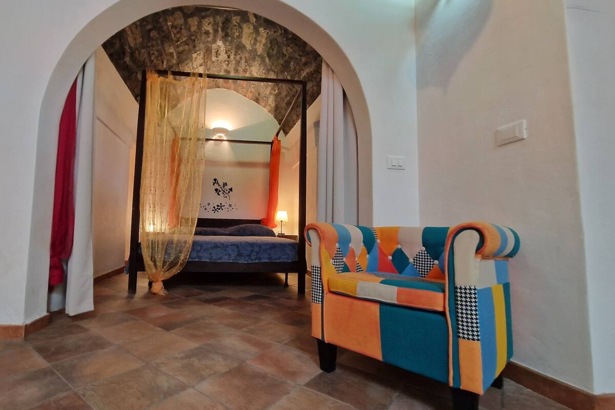 Ein Schlafzimmer mit einem Bett, einem farbenfrohen Sofa, einem Rundbogen und einer Wand mit Dekoration.