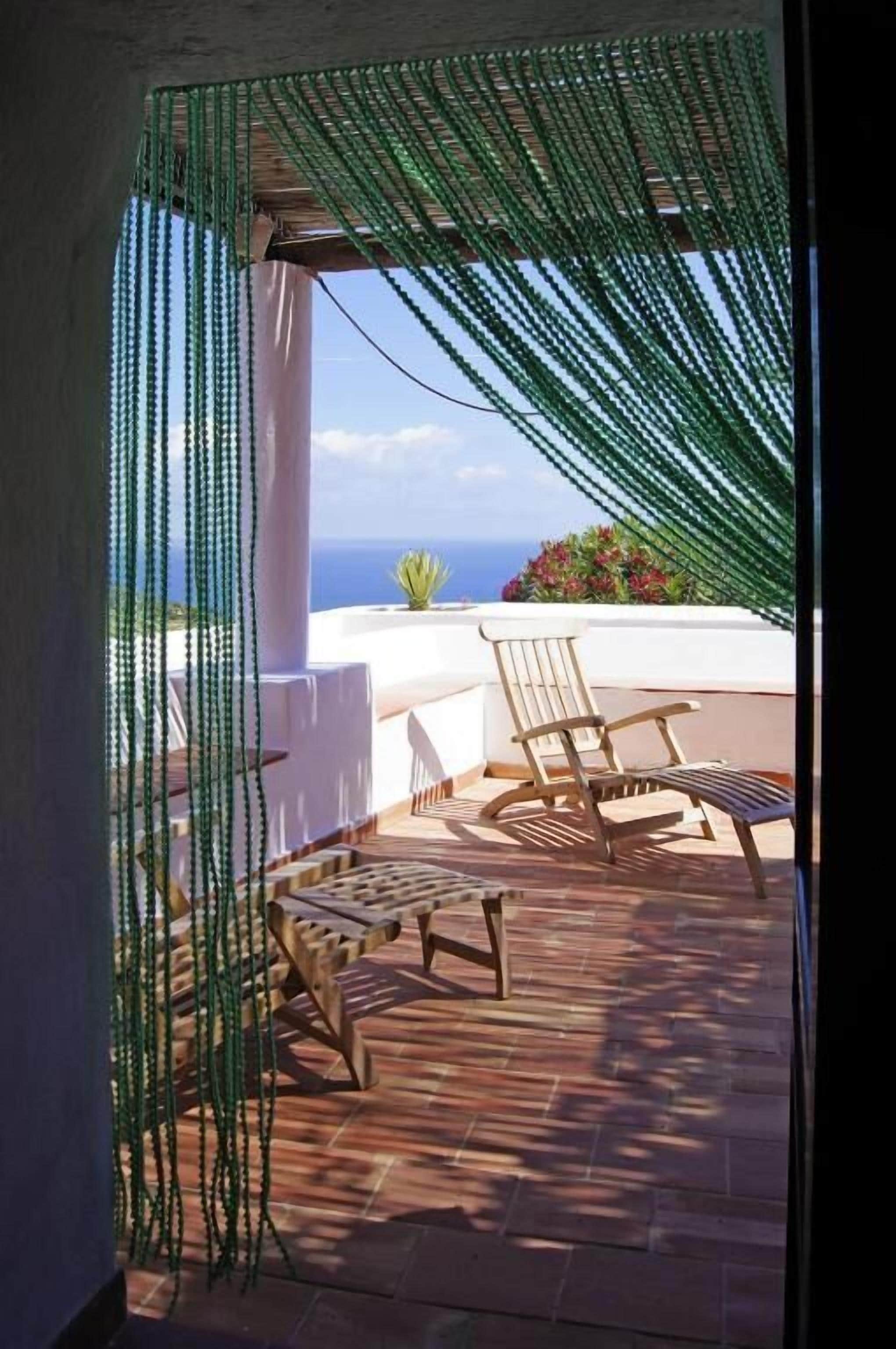 An outdoor patio with a view of the sea, a wooden table, and two chairs.