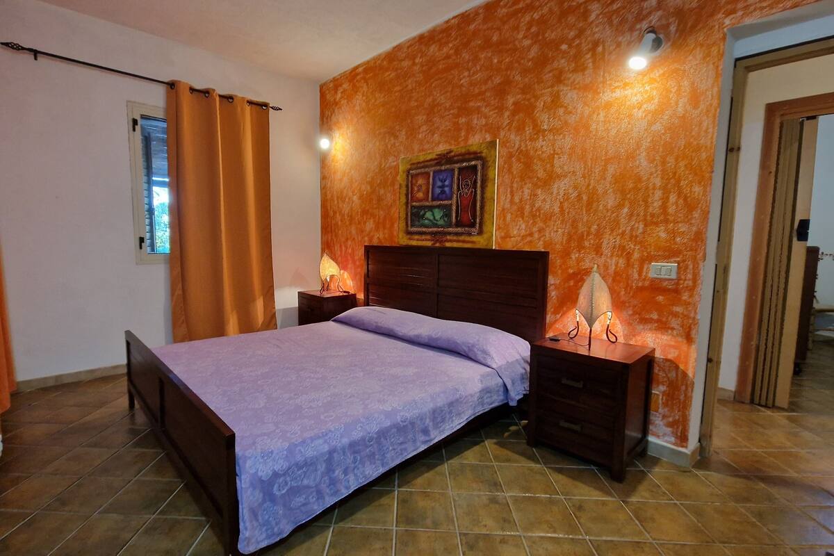 Ein Schlafzimmer mit Bett, Nachttischen, einer Wandlampe und einem Fenster mit Vorhängen.