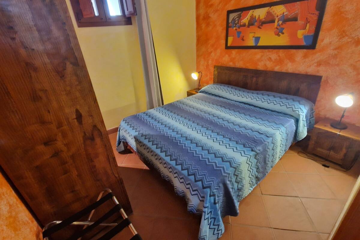 Ein Schlafzimmer mit einem Bett, einer Holztür, einem Nachttisch mit Lampe und einem Bild an der Wand.