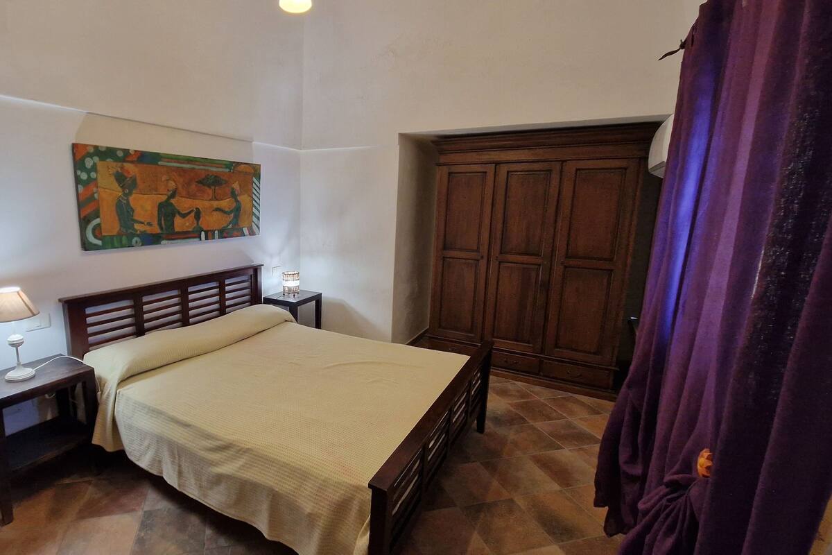 Ein Schlafzimmer mit einem Bett, einem Nachttisch, einer Lampe, einem Gemälde und einem Kleiderschrank.