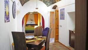 Una habitación con una cama, una mesa de comedor con sillas, un reloj y una puerta que da a otra habitación.