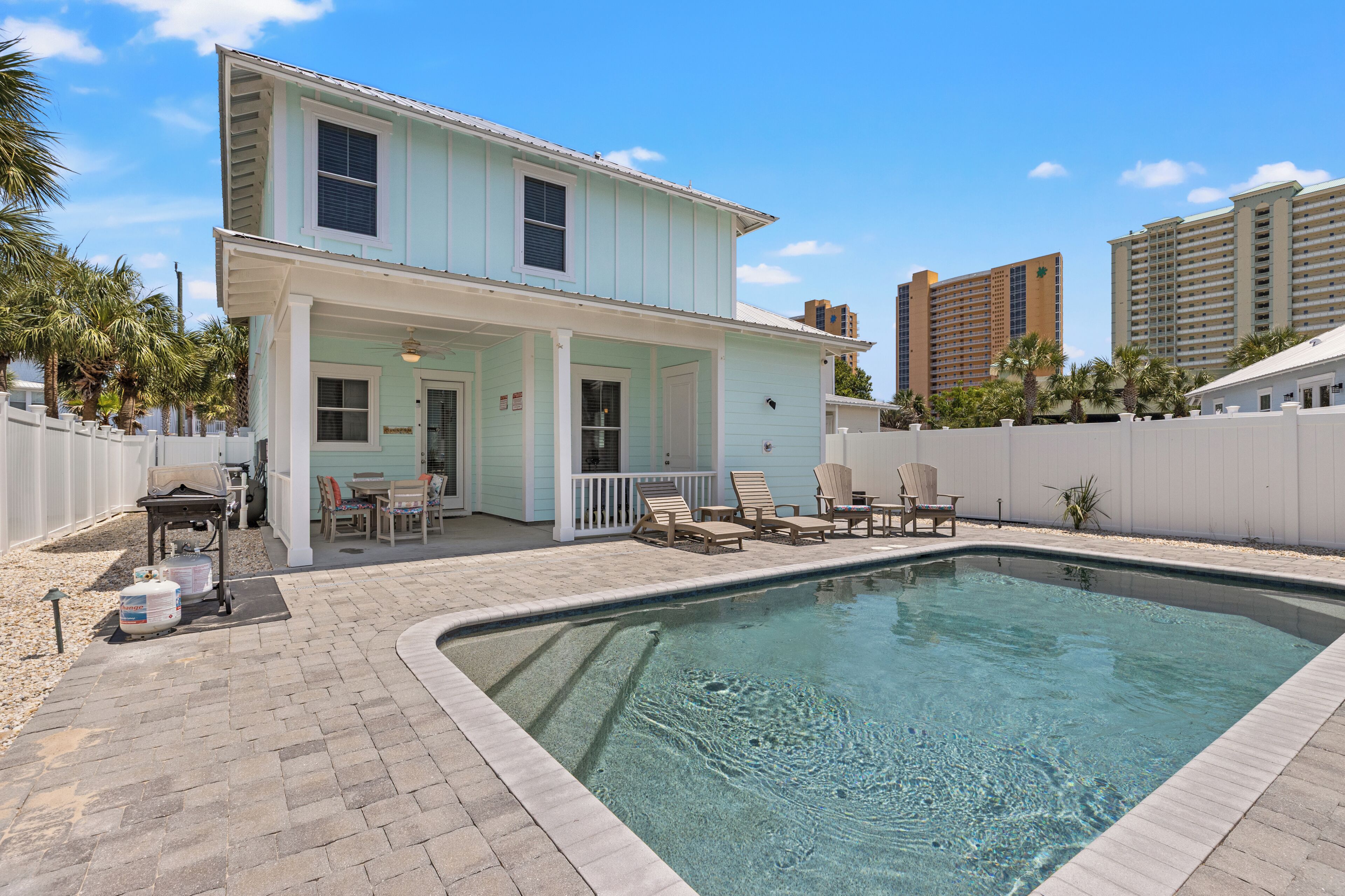 A two-story building with a pool, outdoor seating, and a white fence.