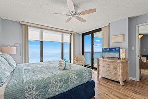 Ein Schlafzimmer mit Bett, Deckenventilator, Kommode, Fernseher und Meerblick.