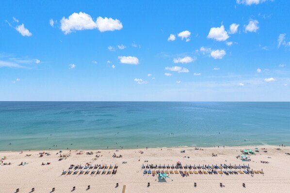 Ein Strand mit Reihen von Liegestühlen und Sonnenschirmen, bewölkter Himmel und ruhiges Meer.